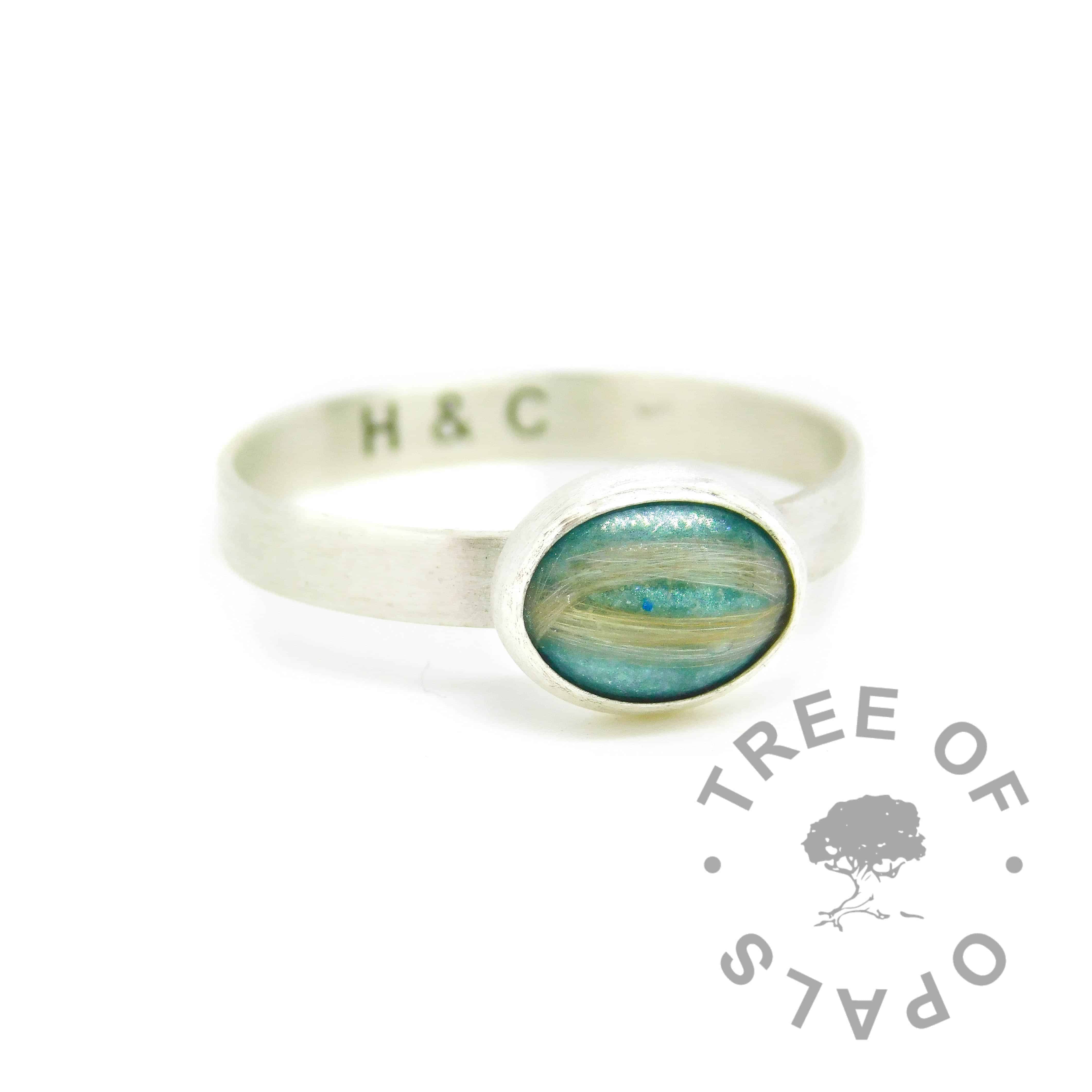 Fur ring with mermaid teal resin sparkle mix, no birthstone, two different dogs' fur. 925 stamped 3mm wide handmade brushed ring band (matte) and 10x8mm bezel cup, handmade with solid sterling EcoSilver. Initials engraved inside in Arial font. Watermarked copyright Tree of Opals memorial jewellery image