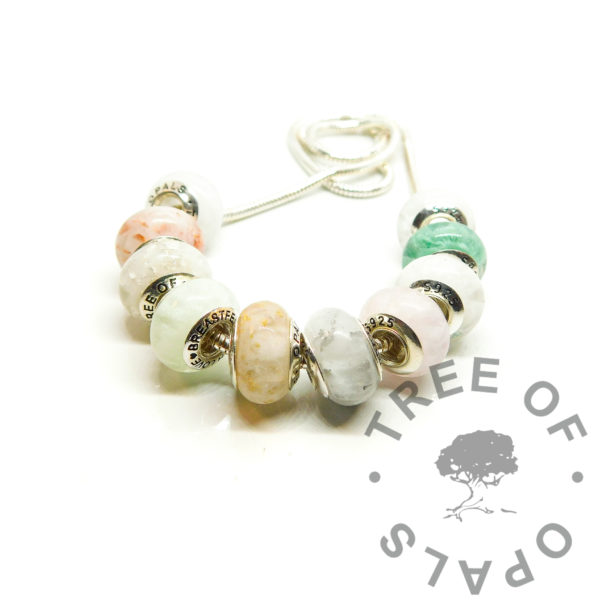 breastmilk beads on snake chain necklace. Breastmilk beads set of ten boobie awards. Left to right: 1. classic breastmilk 2. breastmilk with copper leaf for three month boobie award 3. breastmilk with silver leaf for six month boobs 4. breastmilk and jade resin sparkles subtle green pearlescent with a little angelic aqua for nine month nursiversary 5. breastmilk with gold leaf for one year breastfeeding milestone 6. milk bead with platinum leaf for eighteen month boobies 7. breastmilk and pearlescent pink with a touch of fairy pink for faux morganite to represent breastfeeding a baby with allergies, for example CMPA 8. breastmilk with moonstone effect, purple and blue pearlescent powders and indigo clear opalescent flakes to represent receiving donor milk boobie award 9. faux emerald with amazon jungle green ethically sourced mica and green pearlescent powder for the exclusively pumping breastfeeding award 10. breastmilk with genuine diamond powder